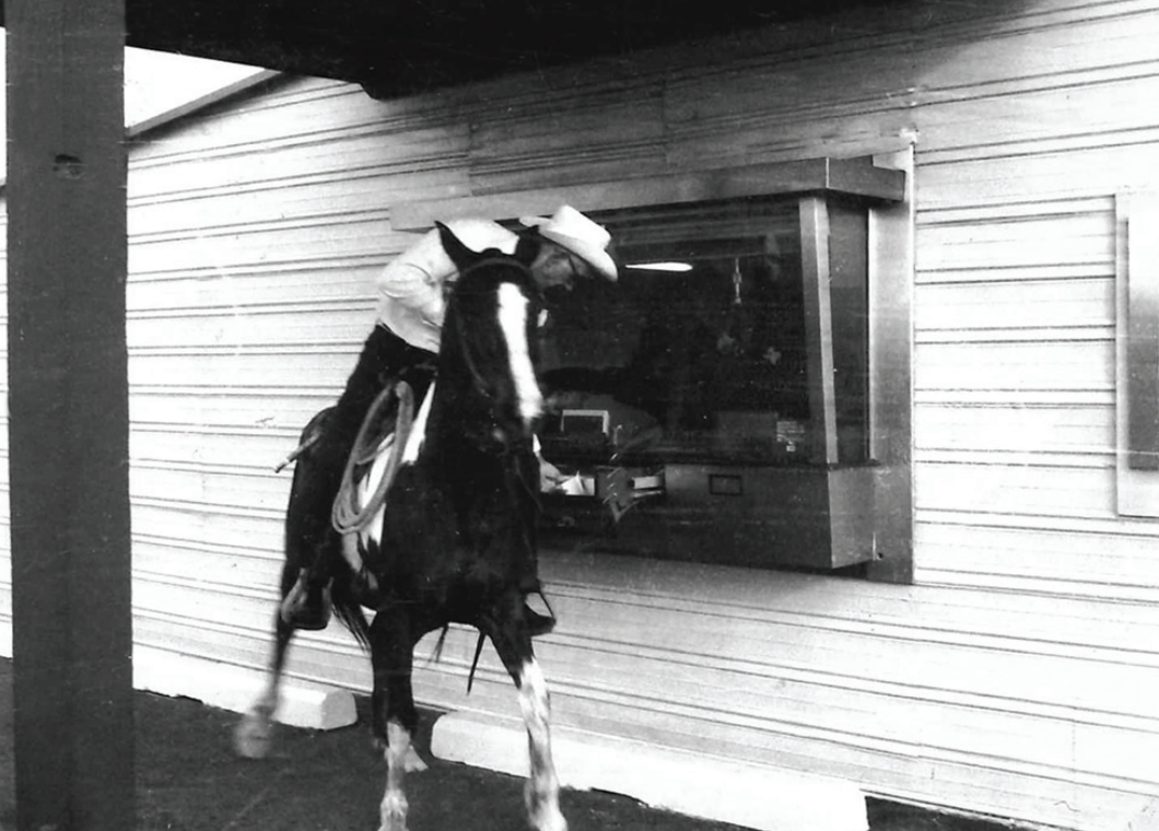 Black and white photo of cowboy at drivethrough with horse