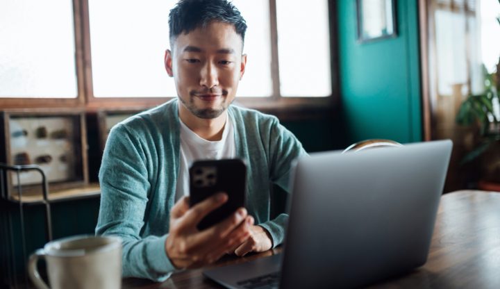 Young man looking at phone and laptop