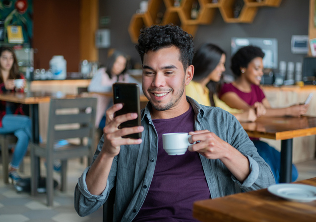 Young man at coffeeshop looking at phone; cybersecurity