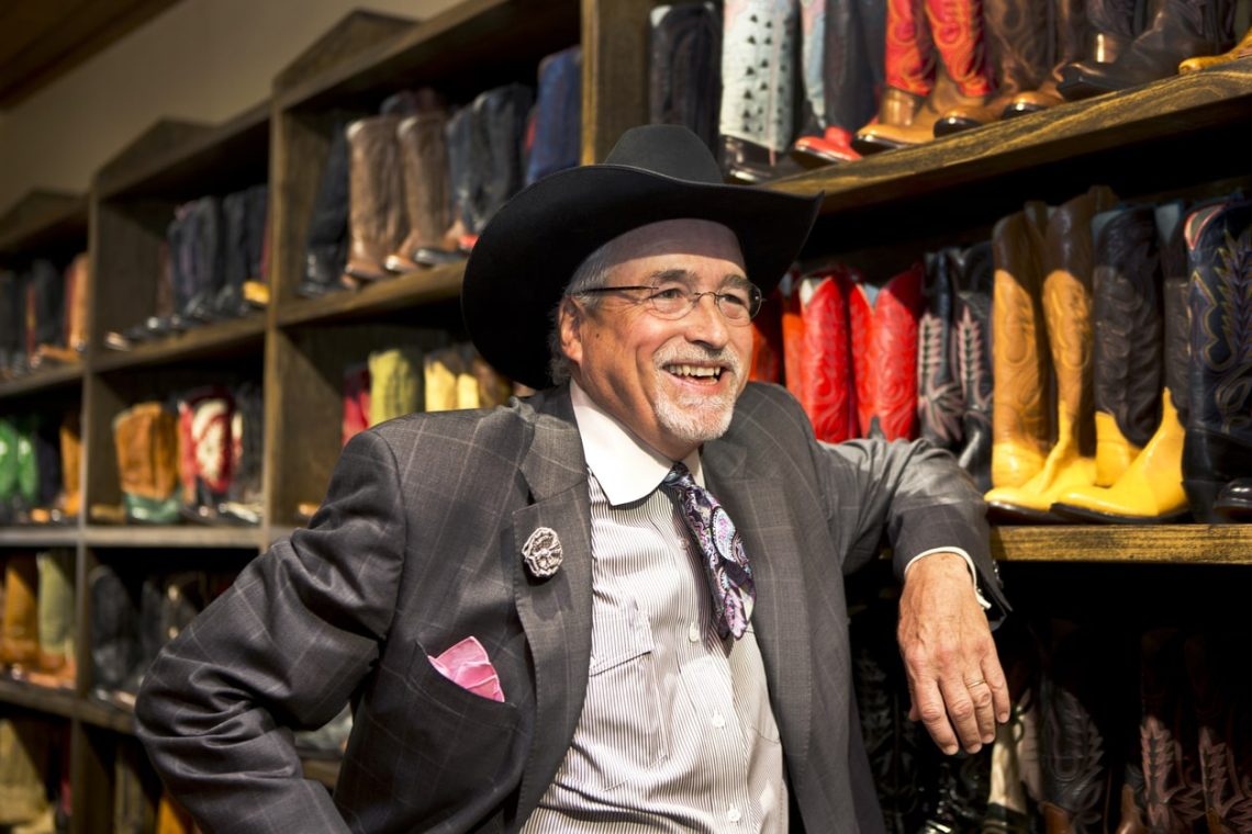 Man with cowboy hat posting in his boot shop